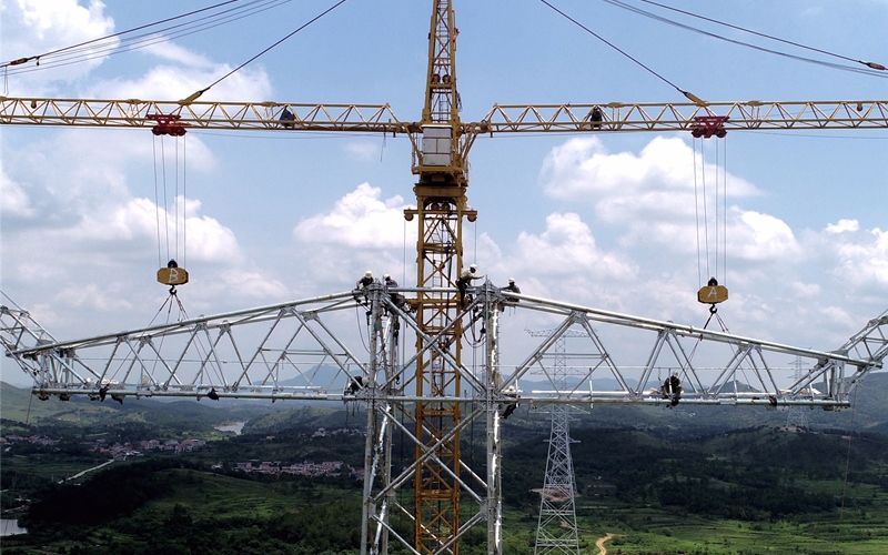 幾名電力施工人員冒著高溫在百米高空安裝塔材。鄒小民攝