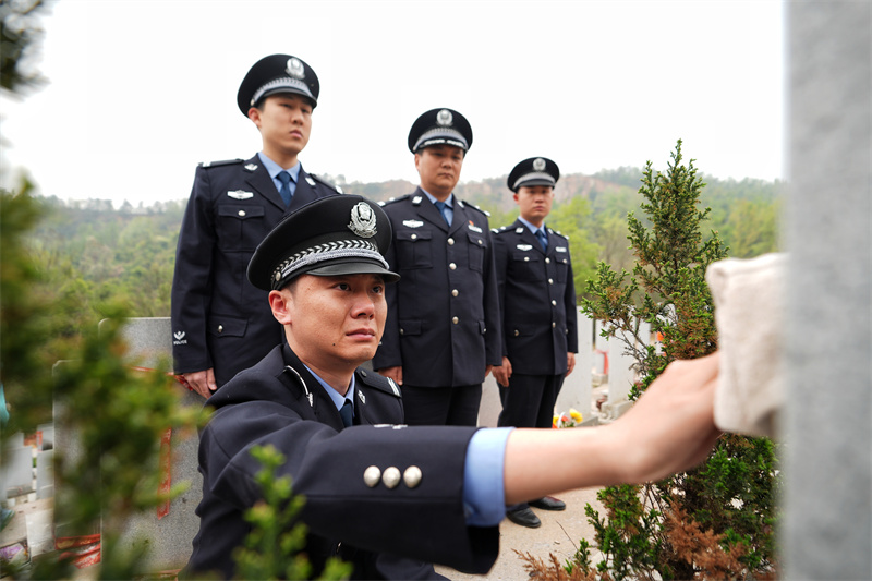 身著警服的鄂靖蹲在父親墓前。