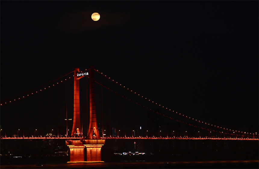 “超級月亮”與鸚鵡洲長江大橋的燈光交相輝映。彭昀迪攝